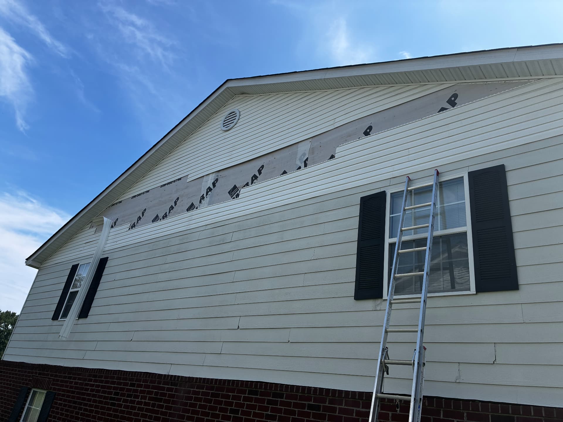 Vinyl siding replacement in progress on a two-story gable, fresh house wrap above the new courses